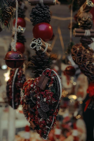 Festive hanging decorations featuring pinecones, red ornaments, cinnamon sticks, and heart-shaped arrangements with red and brown dried flowers.