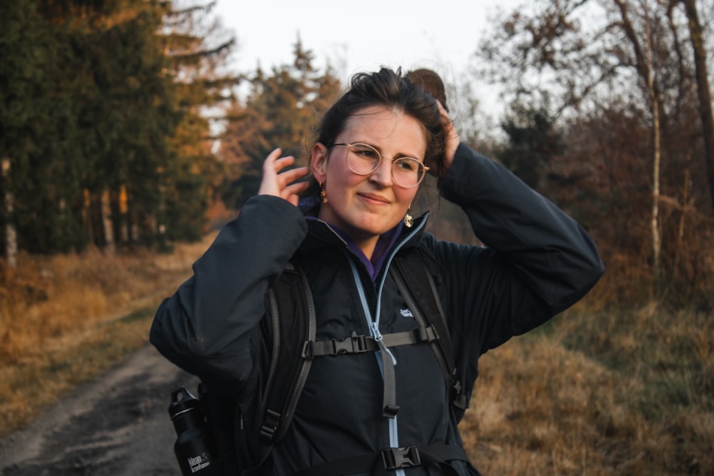 a woman with glasses and a backpack on a dirt road