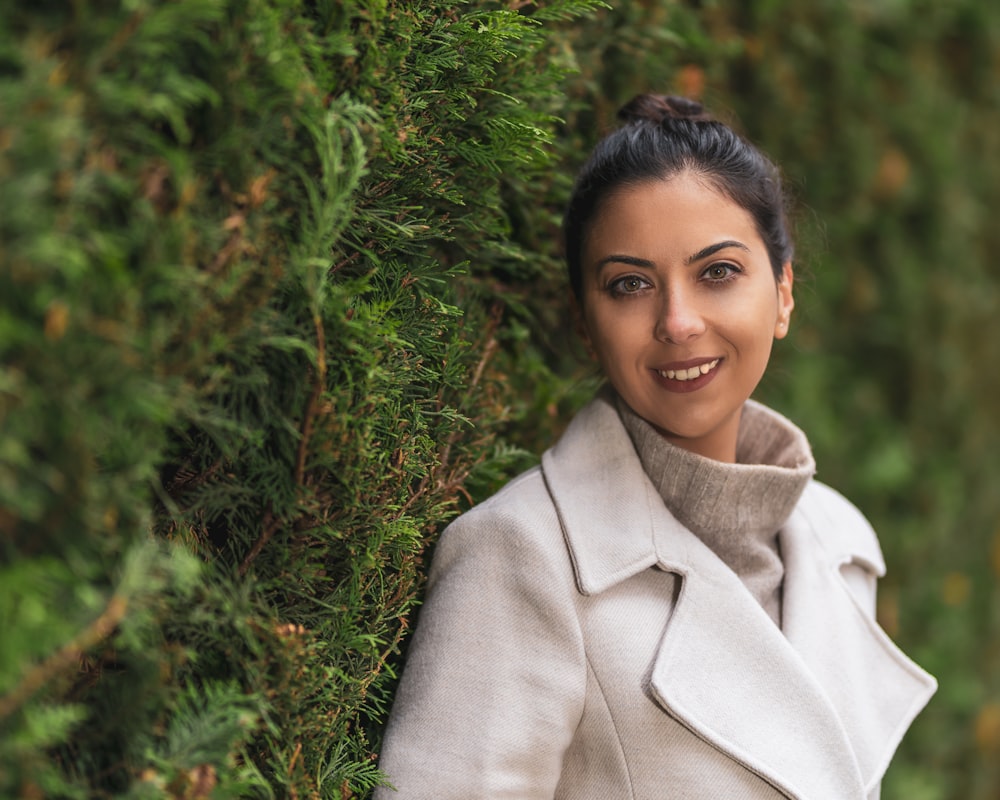 a woman in a coat leaning against a tree