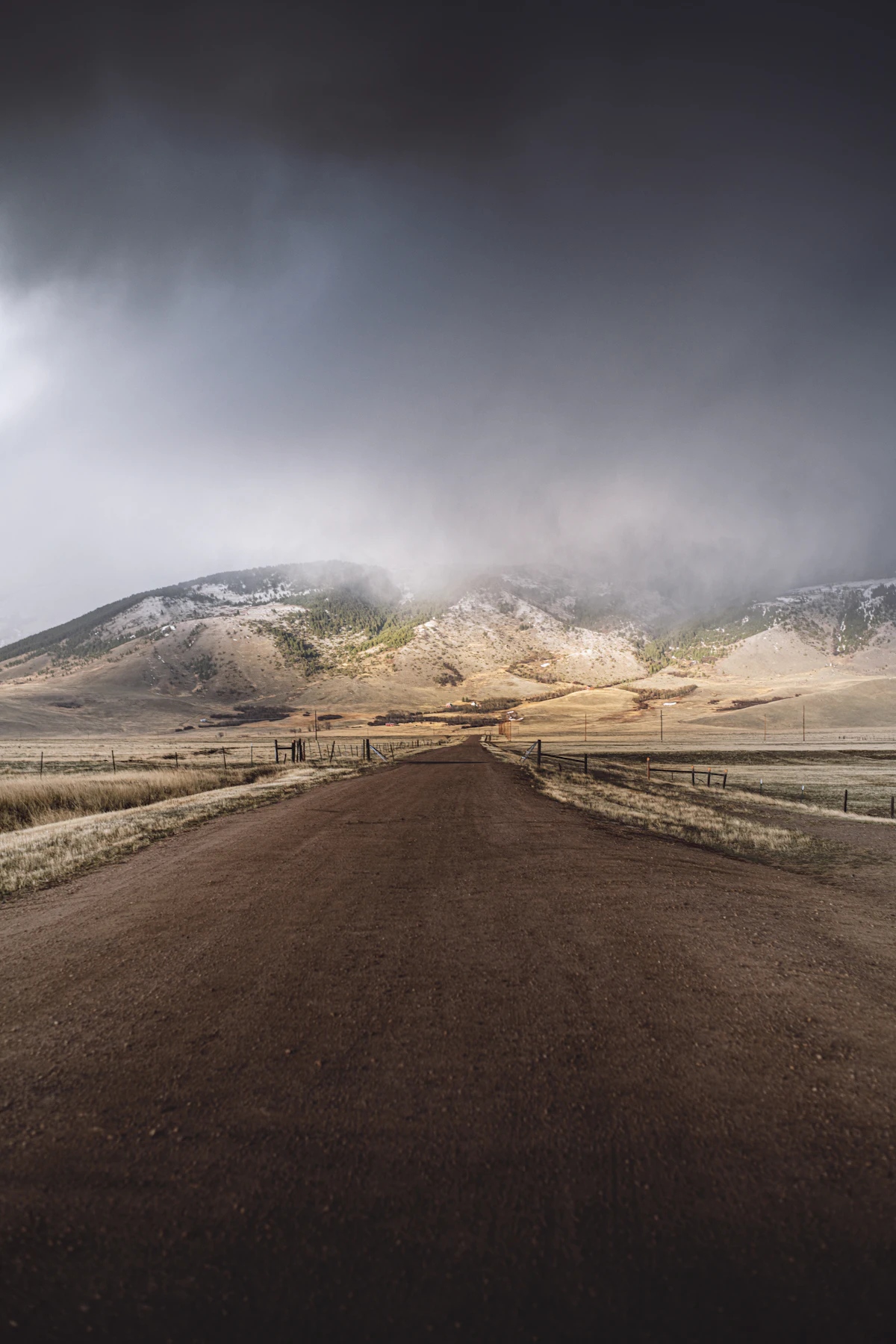 A straight dirt road across dry grassland toward a mountain under storm clouds