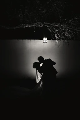 Elegant couple sharing a discreet moment in a softly lit, dark room with violet and pink accents.