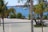 A serene beach scene with palm trees in the foreground and a sandy shoreline. The blue ocean extends into the background, where luxurious overwater bungalows are visible. A couple of boats are anchored near the bungalows, creating a peaceful and relaxing atmosphere.