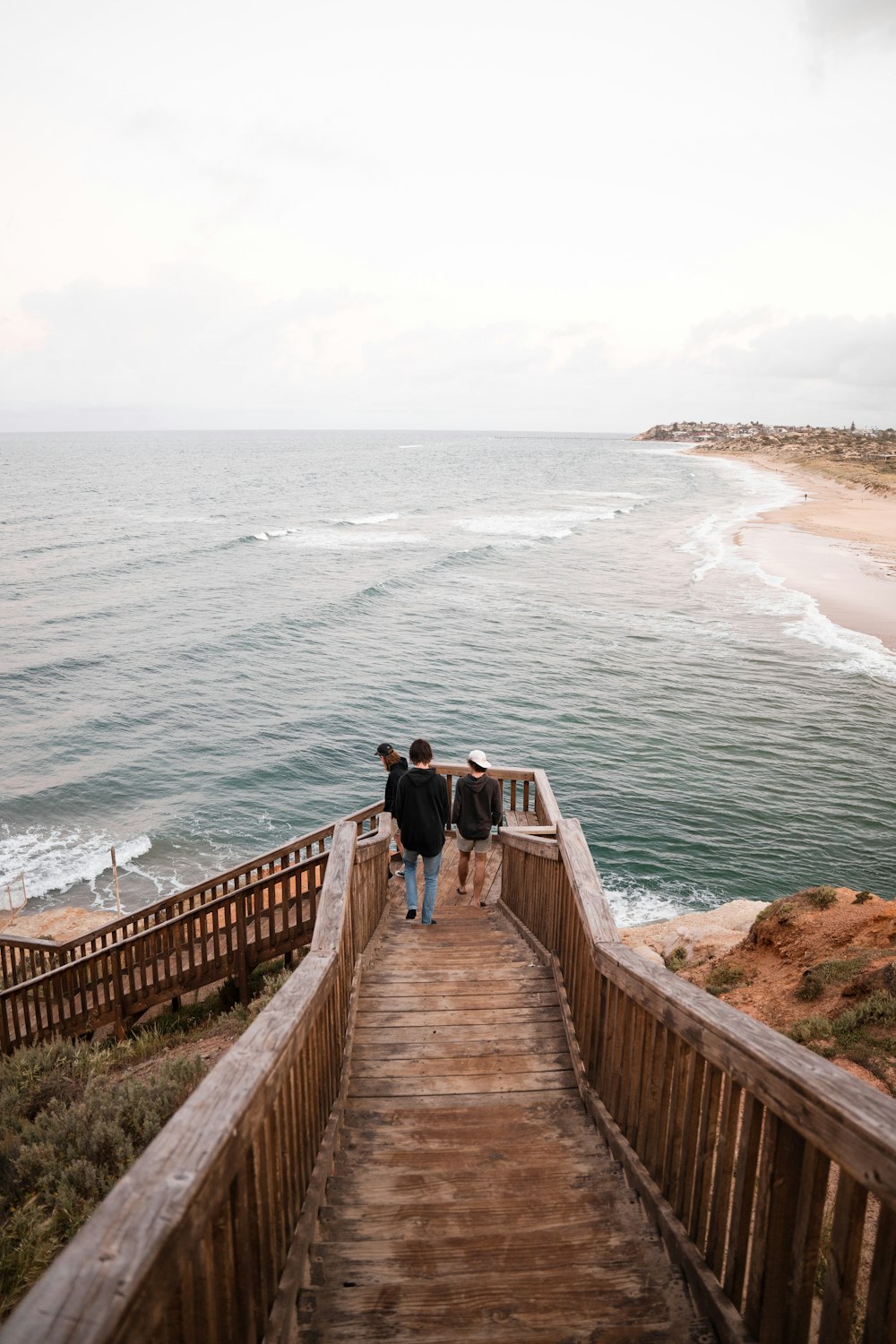 a couple of people walking down a wooden walkway next to the ocean