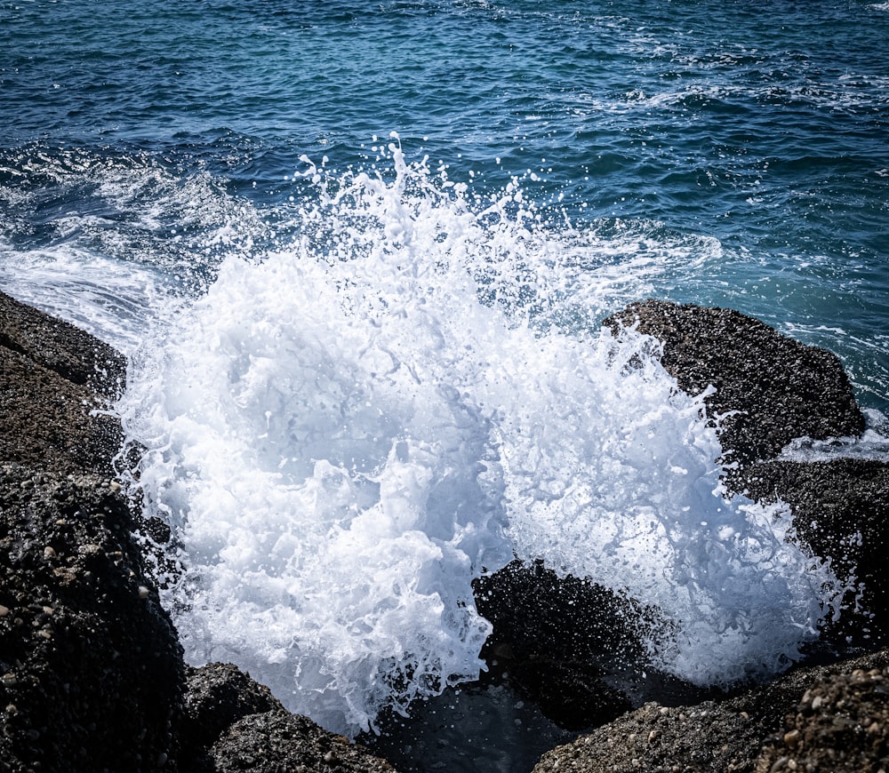 a wave crashes into the rocks near the ocean