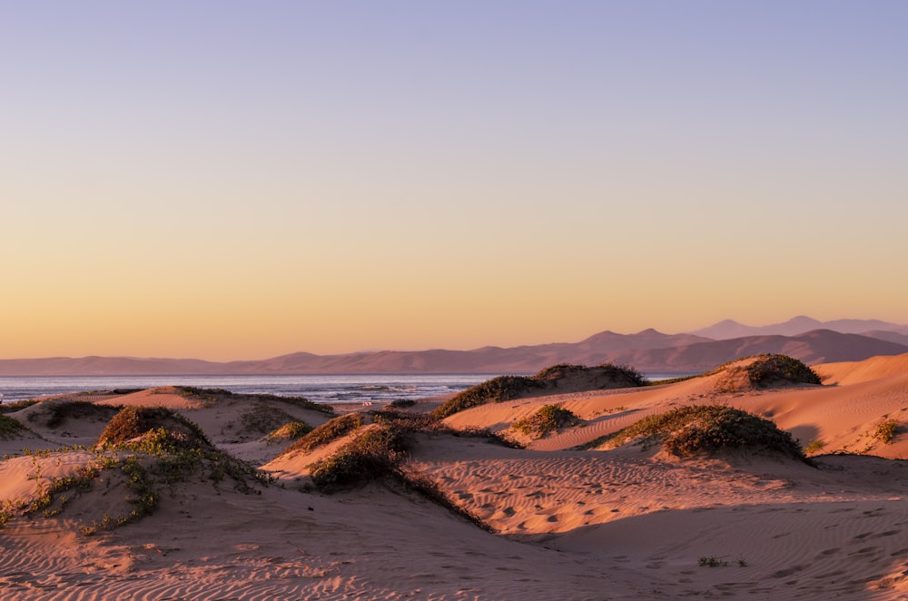 a sandy beach at sunset with mountains in the background