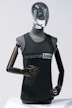 A metallic mannequin with a smooth, reflective head and dark, articulated arms is wearing a sleeveless shirt that reads 'personal trainer'. The mannequin stands upright against a plain light background, emphasizing the sleek design.