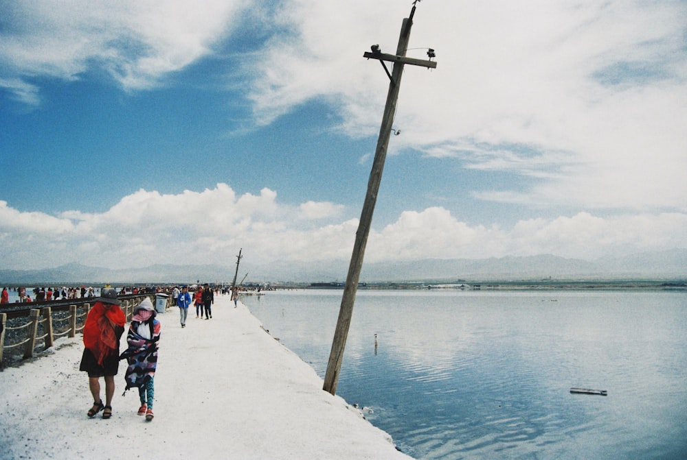 a group of people walking along a pier next to a body of water