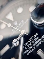Close-up view of a luxury watch face, displaying intricate details including the brand name, model designation, and specifications. The hands and indices are clearly visible with fine craftsmanship, highlighting time-telling elements on a dark, glossy surface.