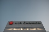 A large building facade with the Air Canada logo prominently displayed. The logo features a red maple leaf within a circle. The building is constructed from reflective materials and the scene is captured under a clear sky, suggesting a modern and corporate environment.