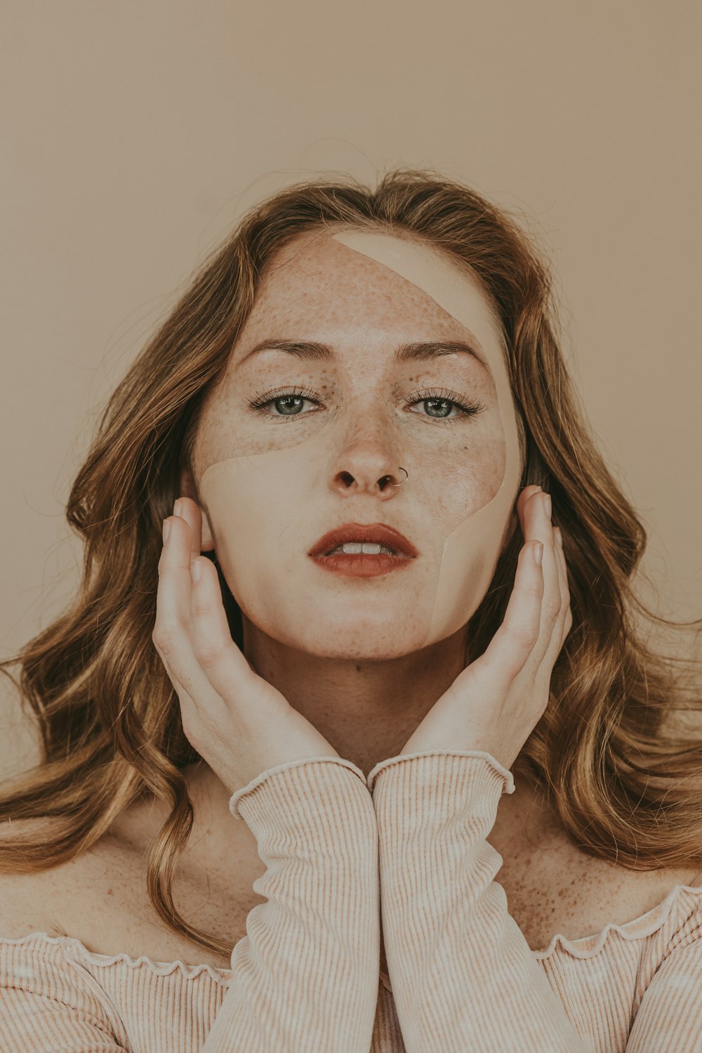 a woman with freckles on her face holding her hands to her face