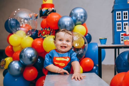a baby sitting at a table surrounded by balloons