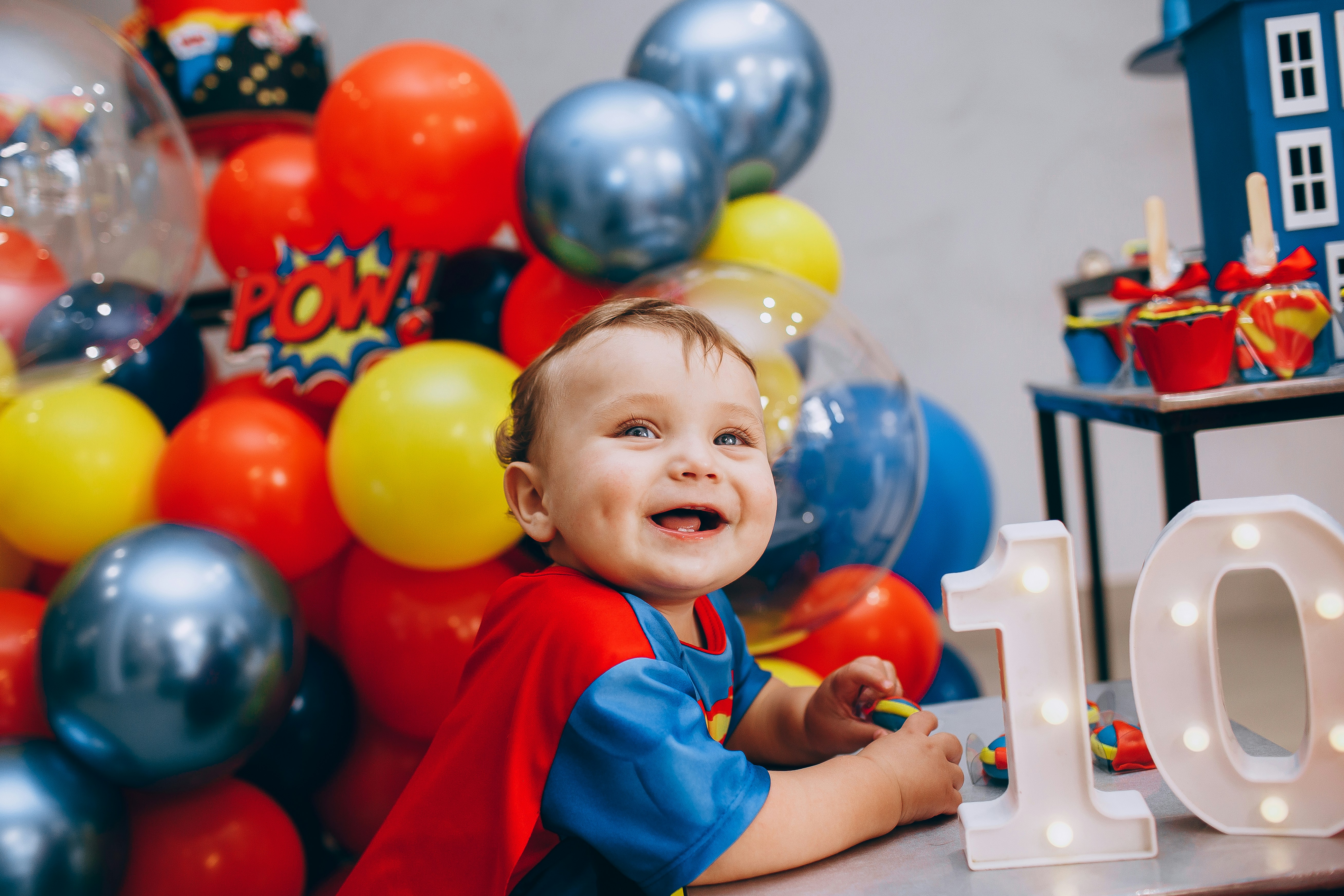 a little boy sitting in front of a table with balloons