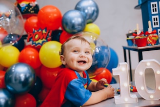 a little boy sitting in front of a table with balloons