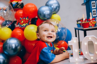 a little boy sitting in front of a table with balloons