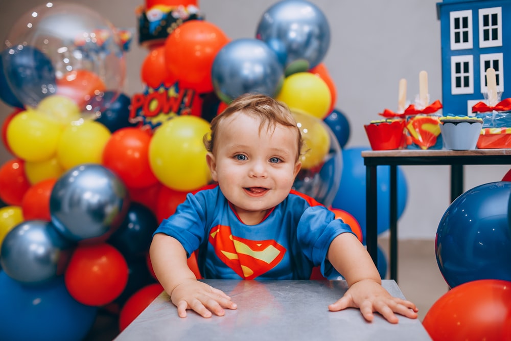 a little boy sitting at a table in front of a bunch of balloons