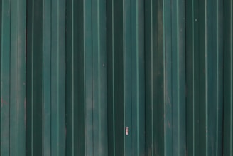 a red fire hydrant in front of a green metal wall
