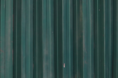 a red fire hydrant in front of a green metal wall