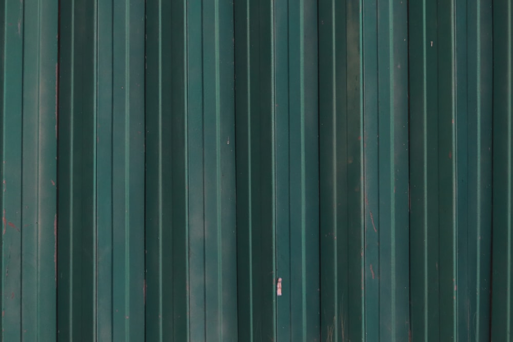 a red fire hydrant in front of a green metal wall