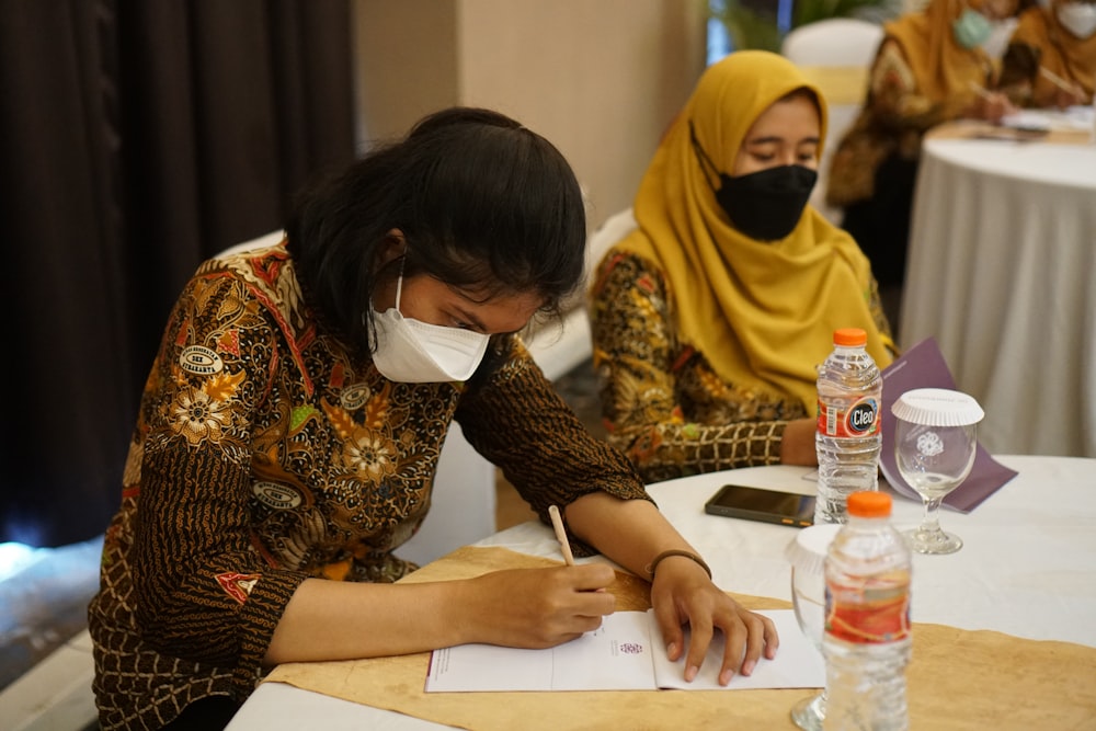 a woman wearing a face mask writing on a piece of paper