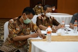 a group of people sitting at a table with masks on