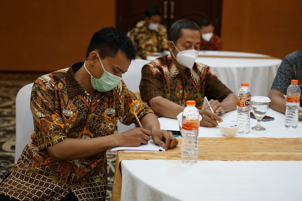 a group of people sitting at a table with masks on
