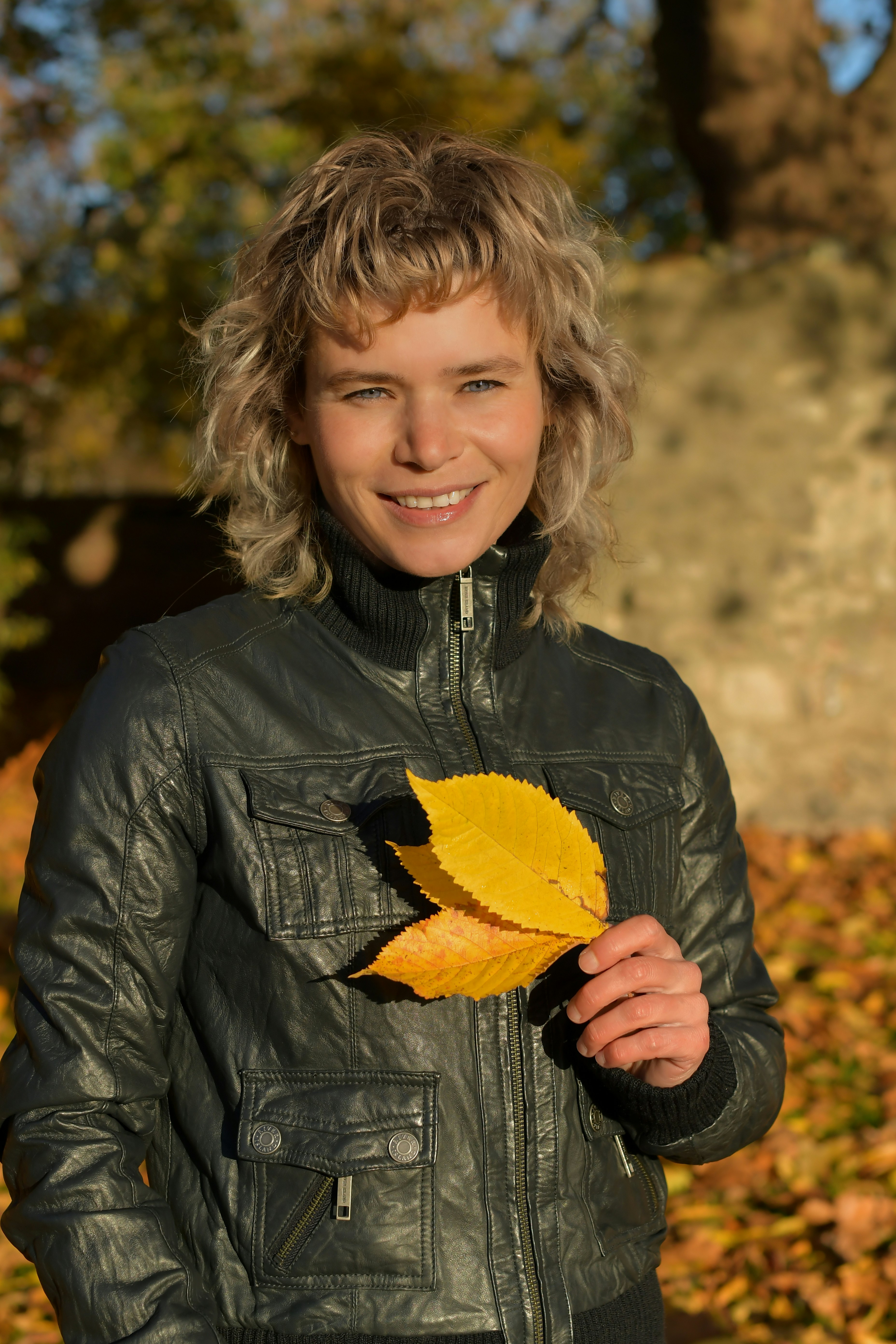 a woman in a leather jacket holding a leaf