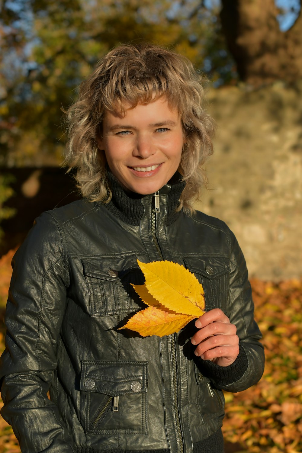a woman in a leather jacket holding a leaf