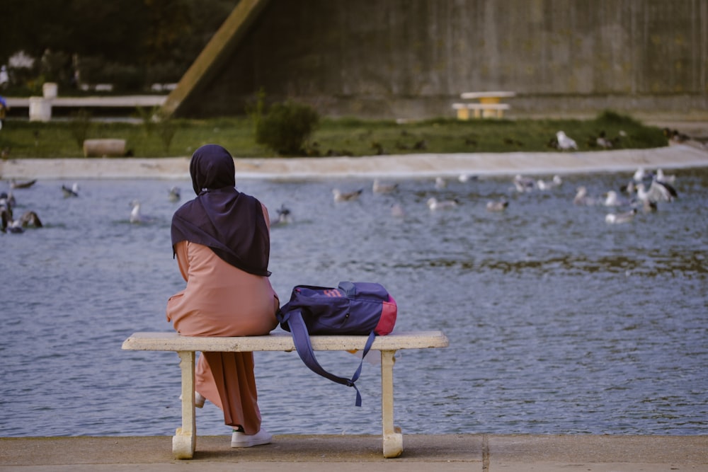 a woman sitting on a bench next to a body of water