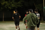 A group of friends laughing and playing on a multi-sport court under string lights.