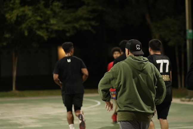 A group of friends laughing and playing on a multi-sport court under string lights.
