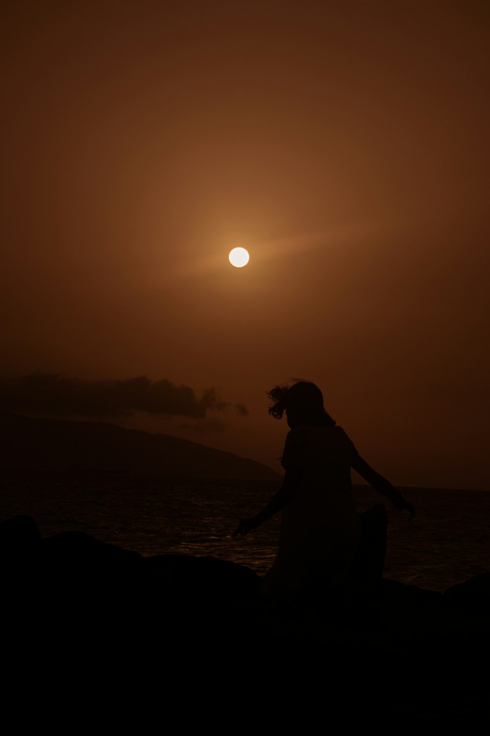 a person sitting on a rock watching the sun set
