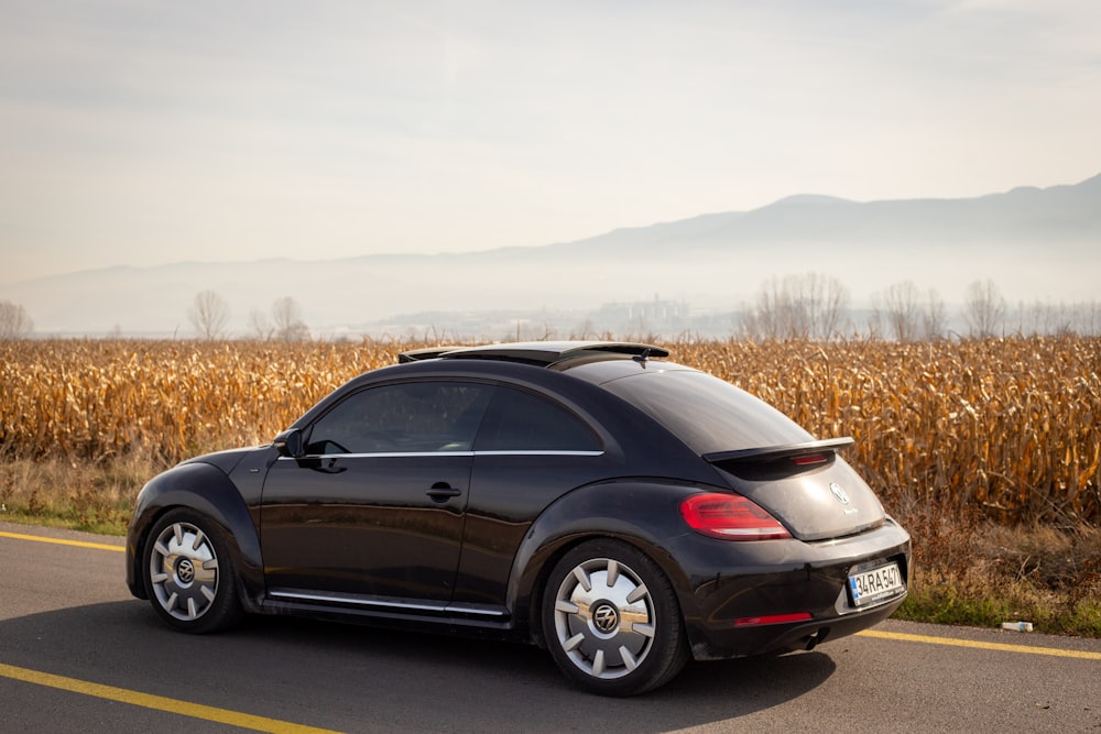 a black car driving down a road next to a corn field