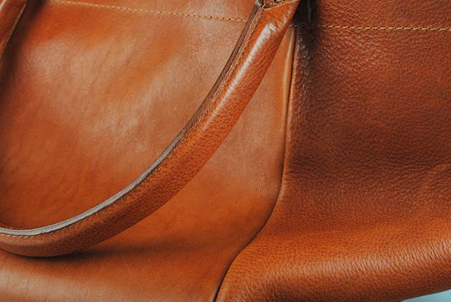 A close-up of a tan leather tote bag with intricate stitching and brass accents.