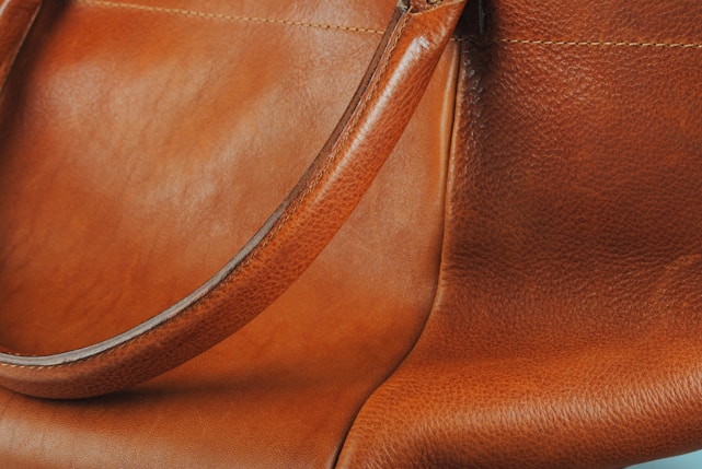 Close-up of a rich brown leather bag with detailed stitching on a dark leather textured background