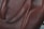A close-up view of a leather surface with a rich, brown texture. The material appears smooth with visible grain patterns, highlighting the quality of the leather. The image captures part of a strap, suggesting it's a piece of leather goods, possibly a bag.