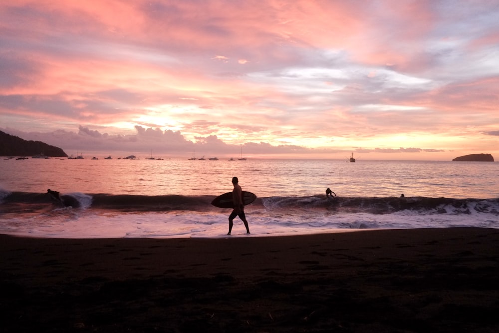 a man holding a surfboard on top of a sandy beach