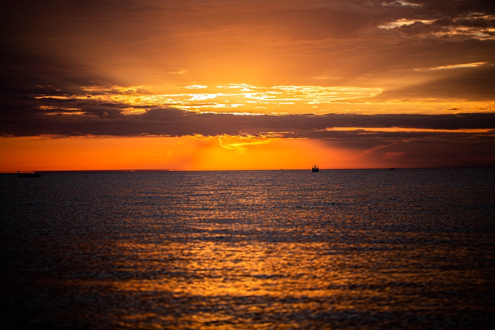 the sun is setting over the ocean with a boat in the distance