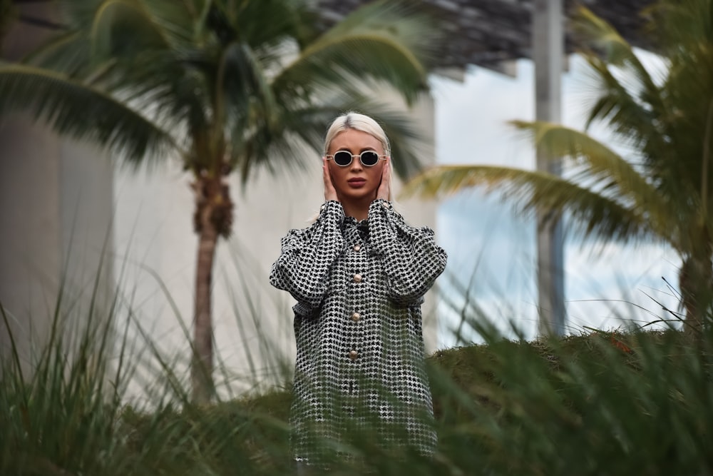 a woman with white hair and sunglasses standing in front of palm trees