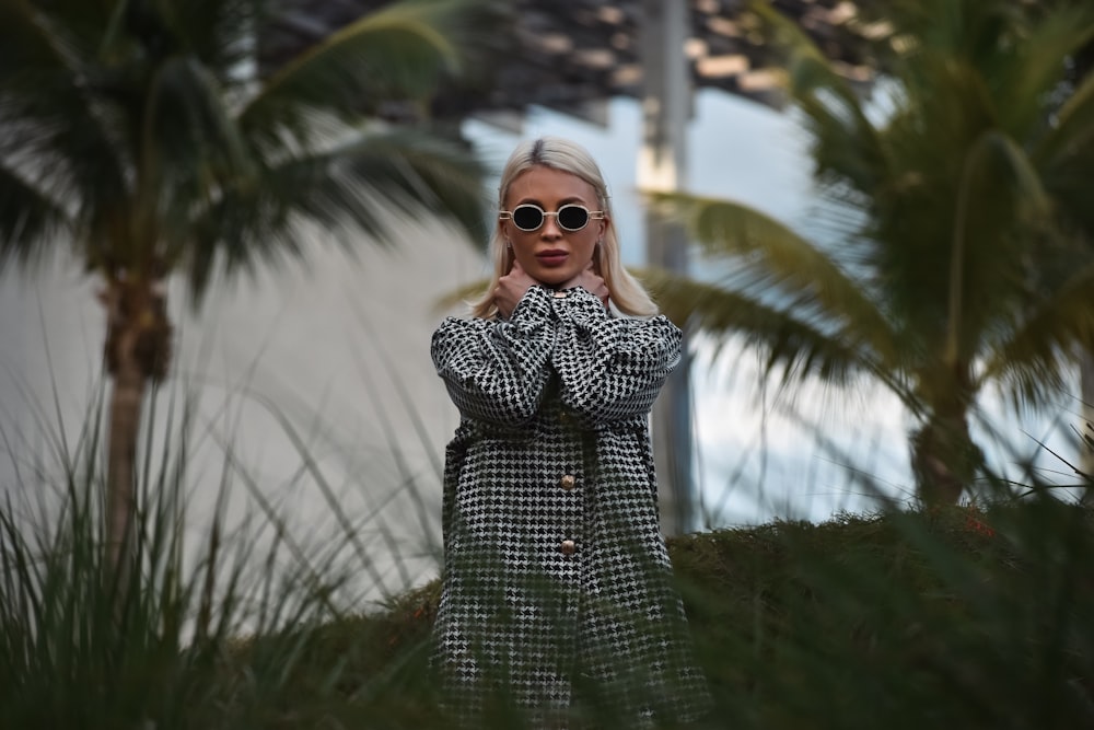 a woman wearing sunglasses standing in front of palm trees