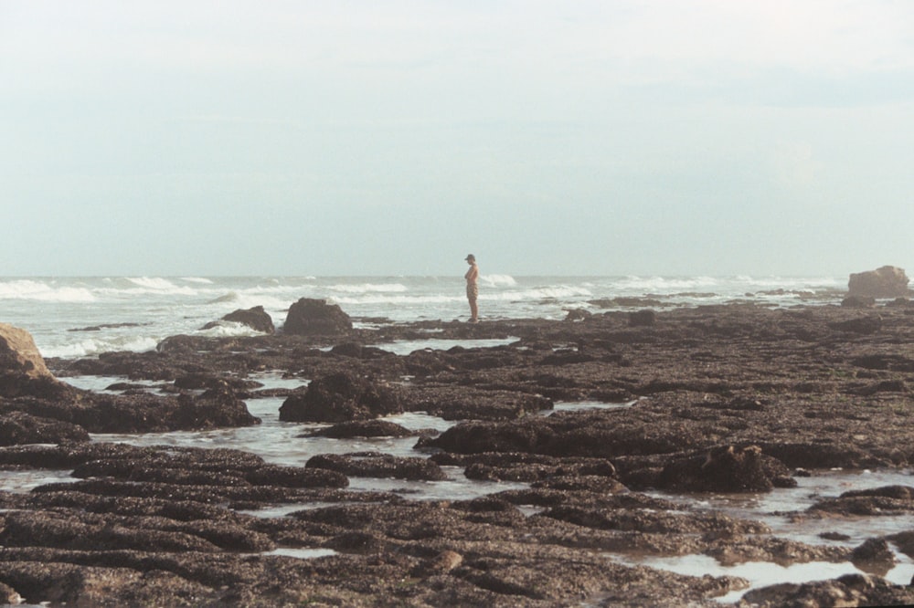 a man standing on top of a rocky beach next to the ocean