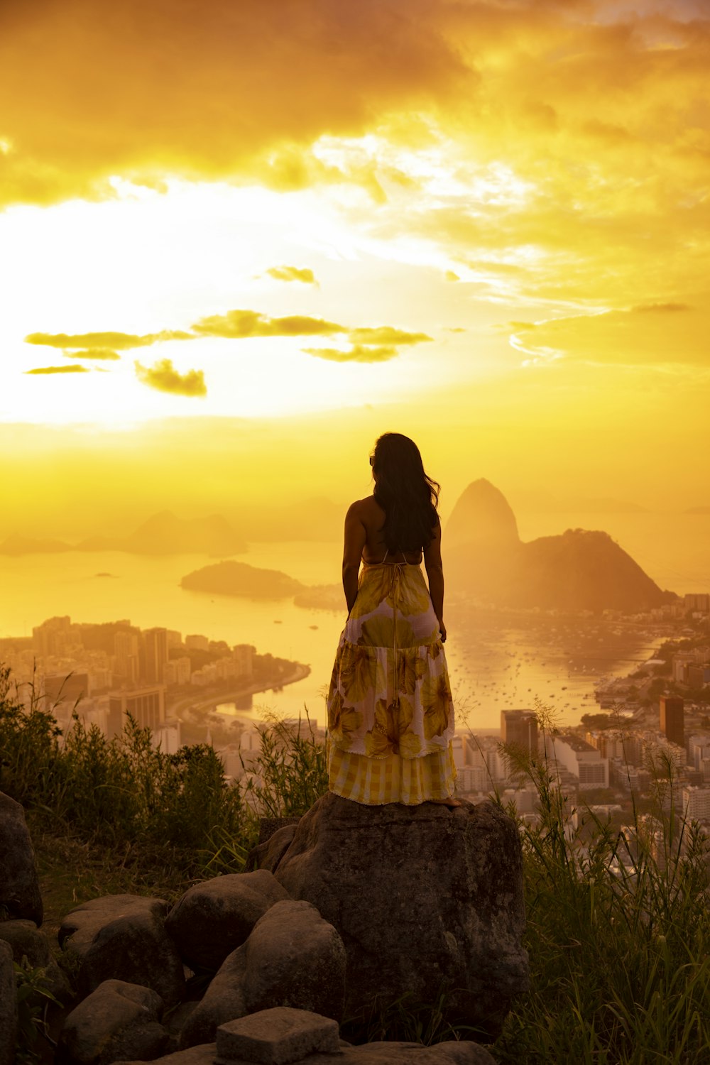 a woman standing on top of a rock next to a lush green hillside