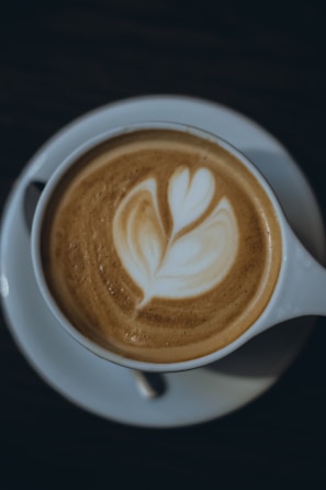 Close-up of a steaming cup of espresso with delicate latte art on a matte black saucer.
