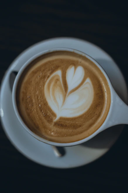 A personalized coffee cup featuring delicate foam art of a floral pattern on a white saucer