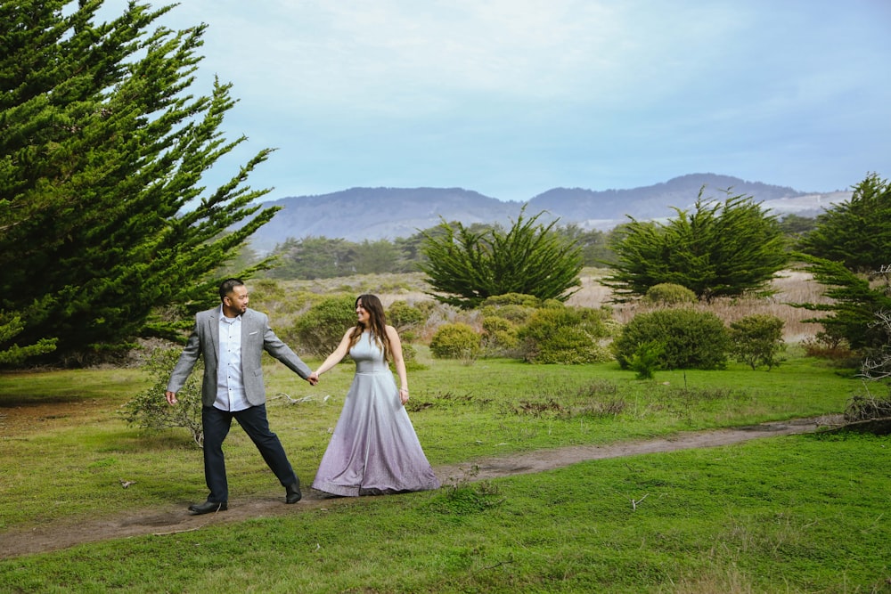 a man and a woman holding hands walking through a field