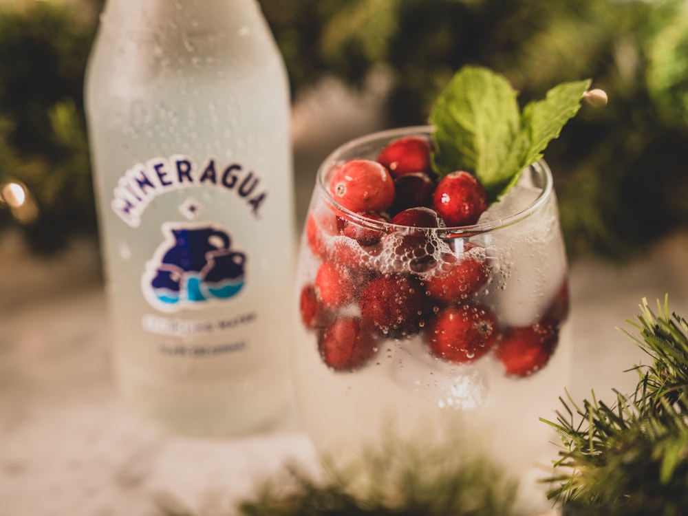 a bottle of mineral water next to a glass filled with berries