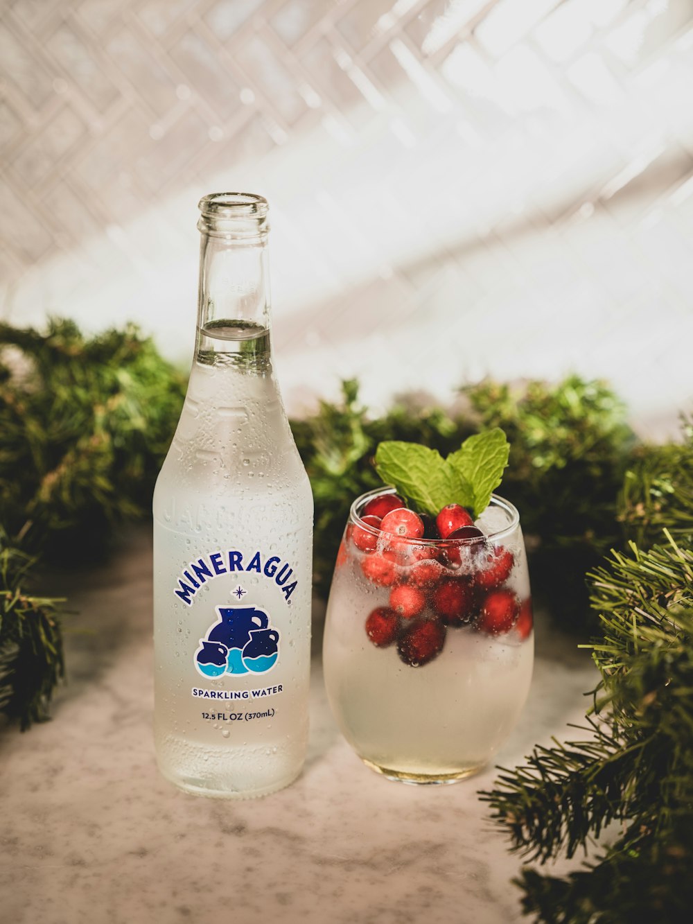 a bottle of mineral water next to a glass filled with berries