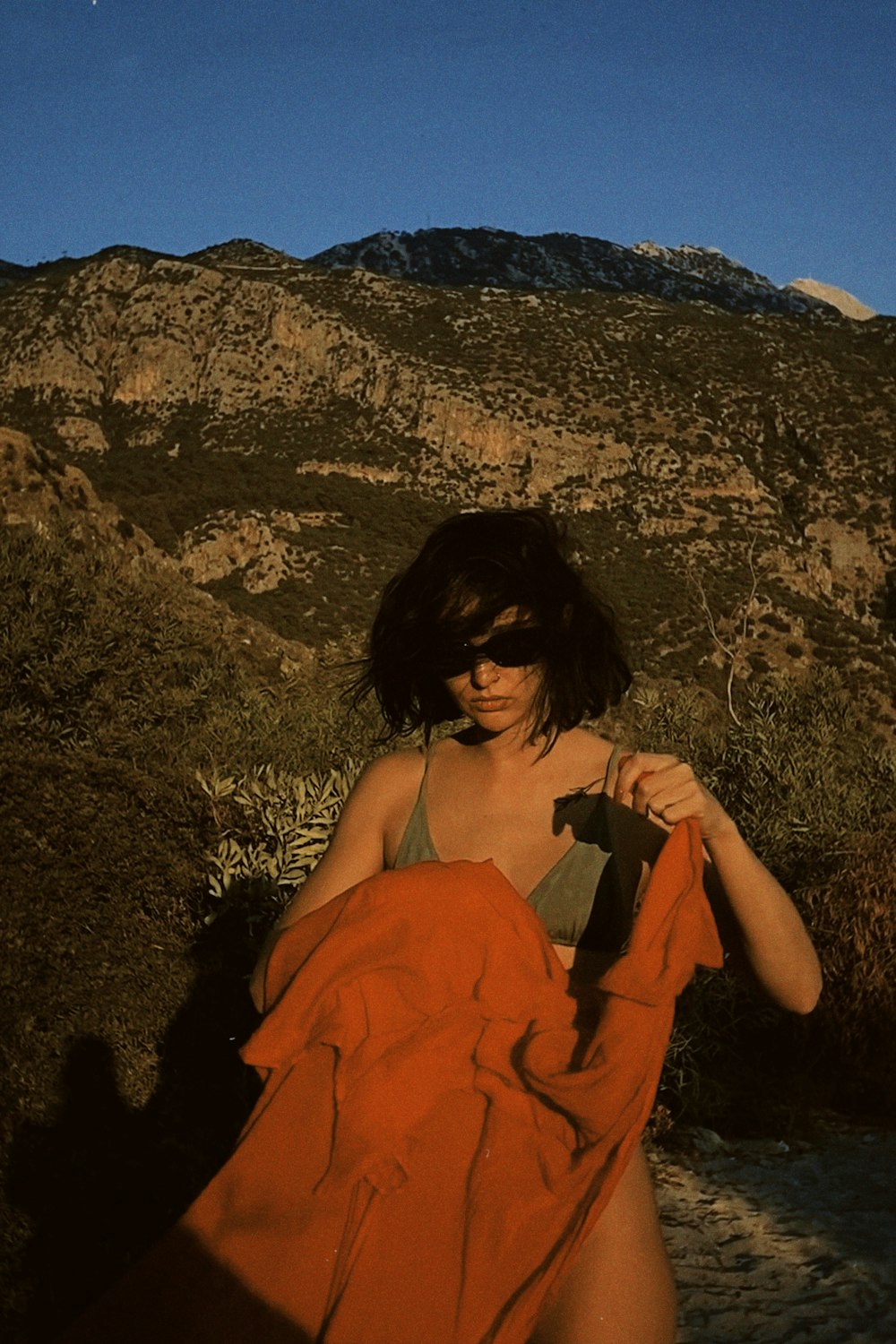 a woman in an orange dress standing in front of a mountain