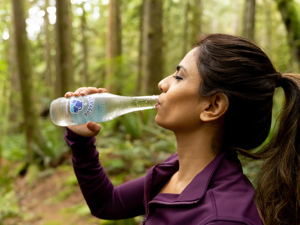 a woman drinking a bottle of water in the woods