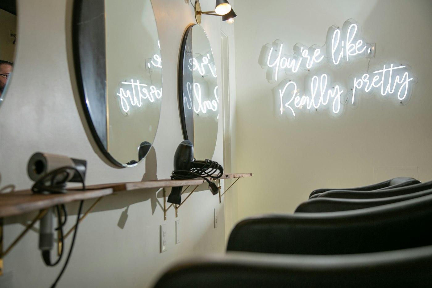 Black styling chairs beneath round mirrors and a white neon sign in a hair salon