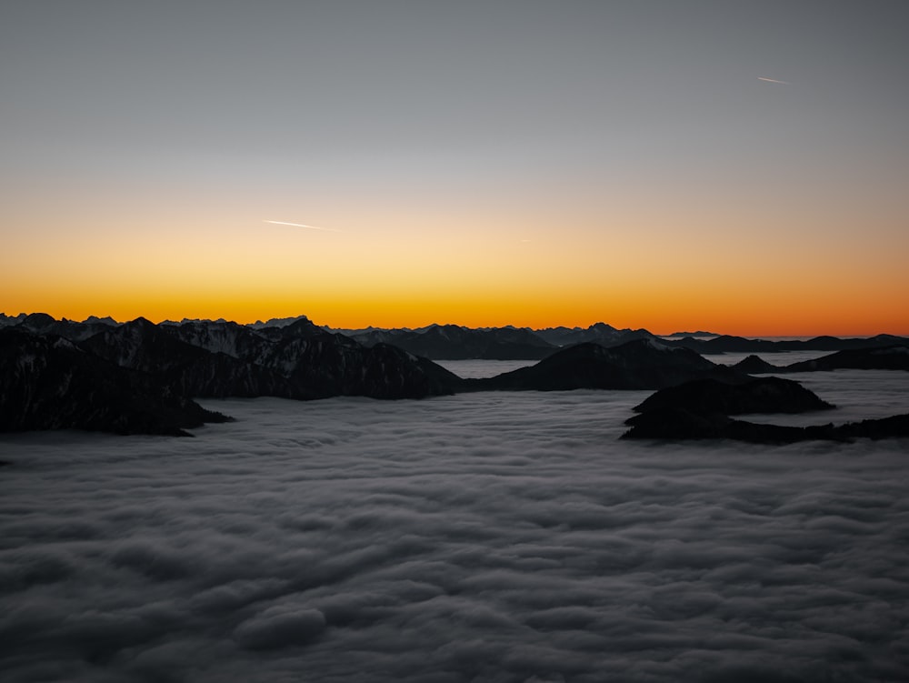 the sun is setting over the mountains above the clouds